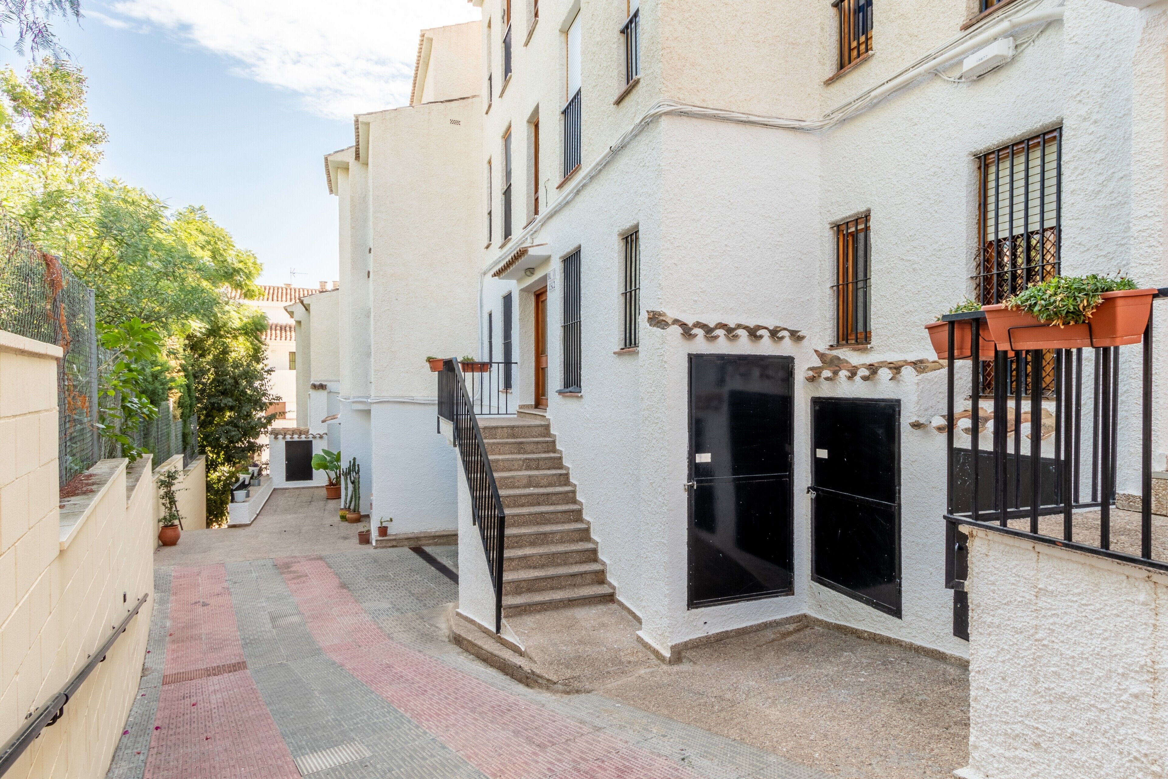 Une rue étroite, bordée de bâtiments des deux côtés, avec un escalier menant à une porte et des plantes en pot sur les balcons.