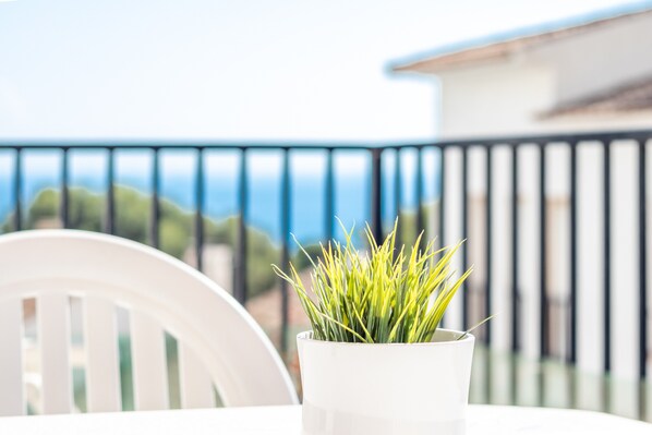 A potted plant on a balcony with a railing and a white chair.