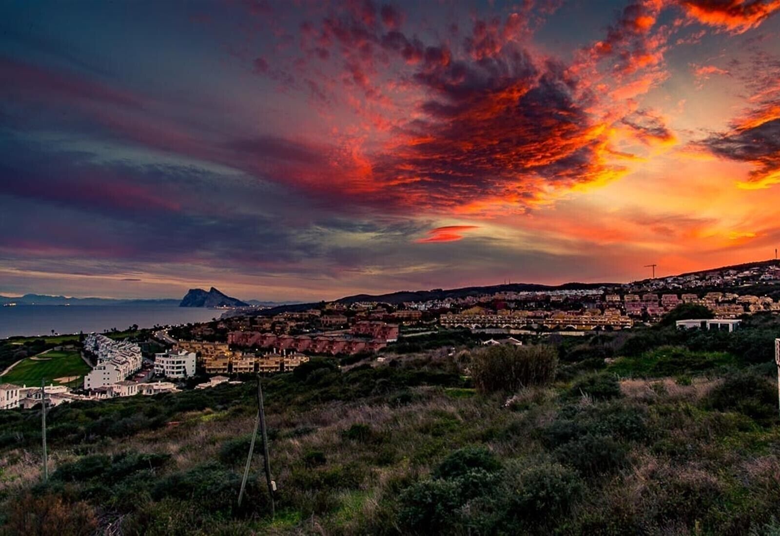 Une ville côtière avec des bâtiments, une colline et un coucher de soleil.