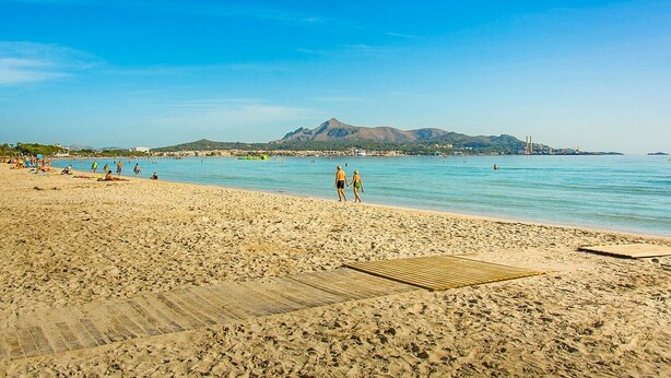 A beach with a wooden deck, clear blue water, and distant mountains.