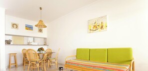 A room with a dining table, chairs, a green sofa, and artwork on the walls.