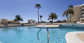A swimming pool with a clear blue water, surrounded by palm trees and buildings.
