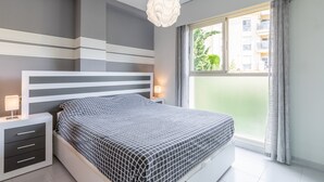 Een moderne slaapkamer met een bed, nachtkastjes, een lamp en uitzicht naar buiten.