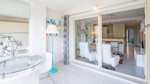 Een moderne woonkamer met een glazen tafel, witte stoelen, een vloerlamp en uitzicht op de keuken.