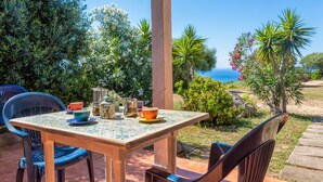 A wooden table with chairs, a view of the sea, and various plants.