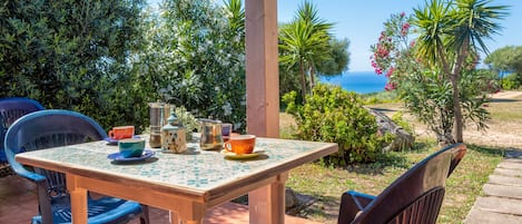 Ein Holztisch mit Stühlen, Blick aufs Meer und verschiedene Pflanzen.