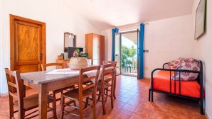 A dining area with a wooden table and chairs, a kitchen area with cabinets, and a bed with a floral bedspread.