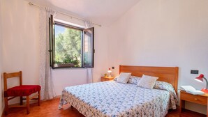 A bedroom with a wooden bed, a chair, a nightstand, a desk, and a window with curtains.