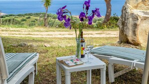 Une table avec une bouteille et un verre à vin, un livre, et une vue sur la mer.