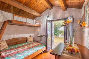 A bedroom with a bed, wooden headboard, a small table with fruit, and a door leading to an outdoor area.