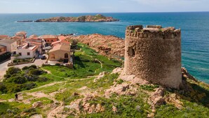 Un village côtier doté d’une tour en pierre, de maisons aux toits rouges et offrant une vue dégagée sur la mer.