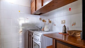 Une cuisine avec des murs recouverts de carreaux blancs, des meubles de cuisine en bois, une cuisinière blanche et un plan de travail en bois.