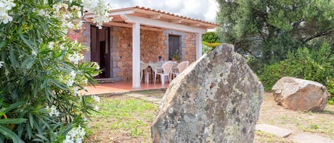 A stone building with a tiled roof, a patio with chairs, and a large rock in the foreground.