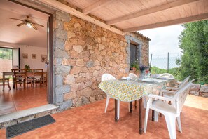 Patio esterno con parete in pietra, tetto in legno e tavolo apparecchiato per consumare un pasto.