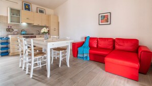 A compact living space with a dining area, a red sofa, and a kitchen with light-colored cabinets.