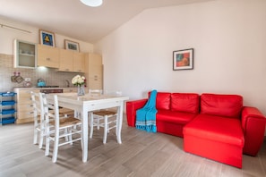 A compact living space with a dining area, a red sofa, and a kitchen with light-colored cabinets.