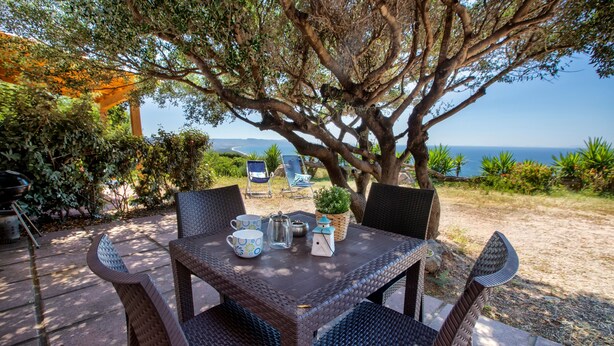 An outdoor dining area with wicker furniture, a table set with a mug, a pitcher, and a small house-shaped container.