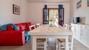 A dining area with a white table, red sofa, and a TV on a cabinet.