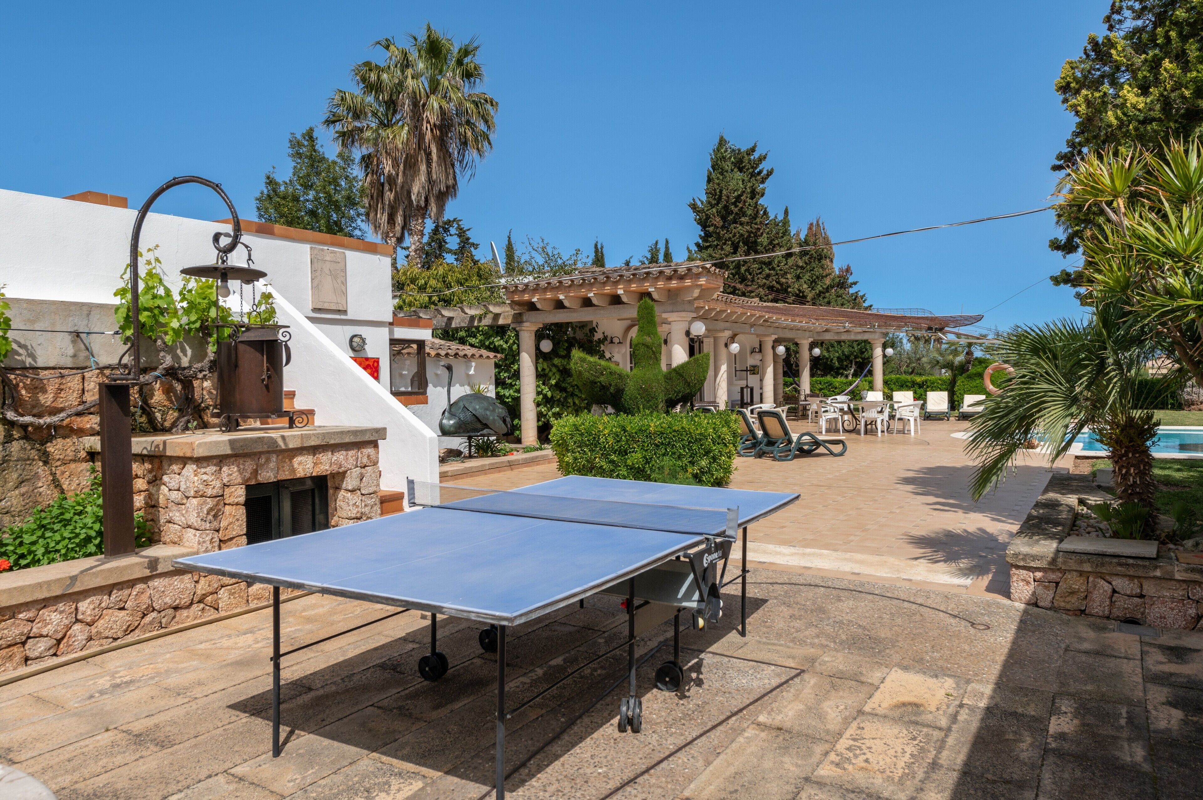 Una mesa de ping pong al aire libre, una chimenea de piedra y un pérgola con asientos.