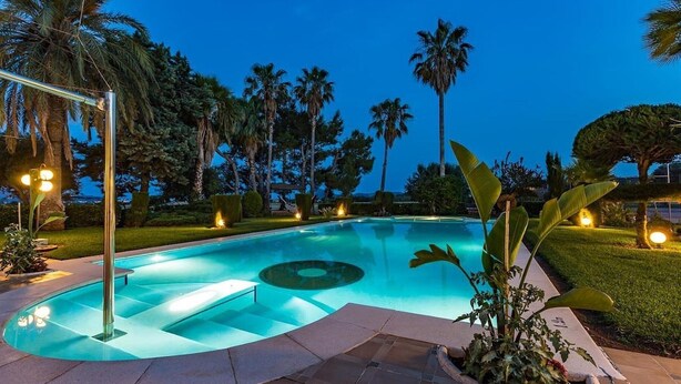 A swimming pool with a circular design, surrounded by palm trees and well-maintained grass. - Villa La Vinya Gran with Mountain View, Sauna, Pool, Jacuzzi, Wi-Fi, A/C, Terraces & Tennis Court (PUERTO DE POLLENSA)
