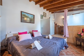 A bedroom with a bed, pillows, a painting, a bathroom, and a wooden ceiling.