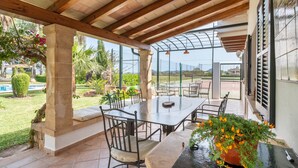 An outdoor patio with a table and chairs, surrounded by plants and a view of the landscape. - Villa La Vinya Gran with Mountain View, Sauna, Pool, Jacuzzi, Wi-Fi, A/C, Terraces & Tennis Court (PUERTO DE POLLENSA)
