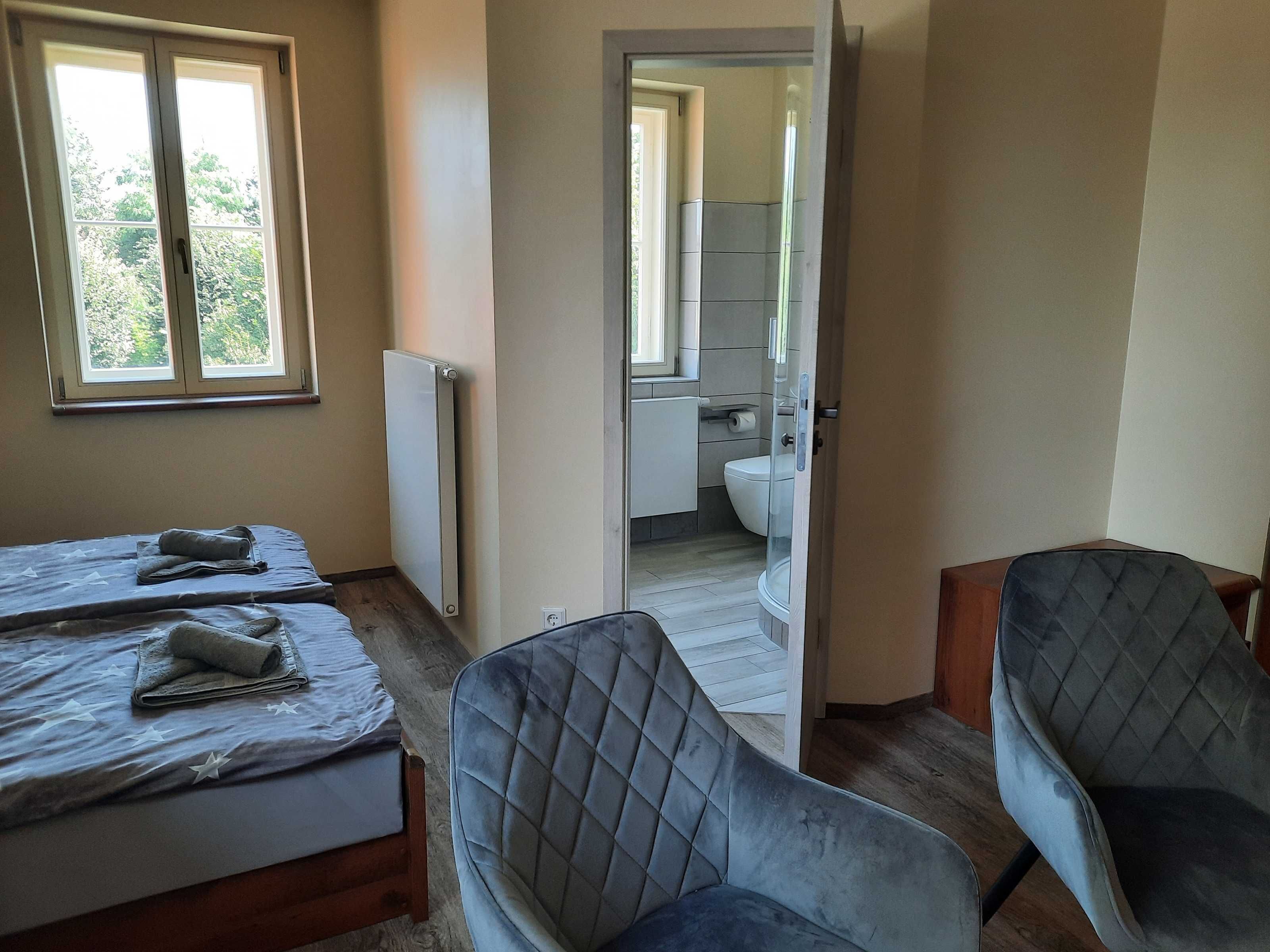 Ein Schlafzimmer mit zwei Betten, einem Heizkörper, einem Fenster und Blick auf das Badezimmer.