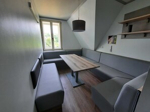 Um espaço de estar moderno e compacto, com um banco embutido, uma mesa pequena e um candeeiro suspenso.