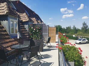 Une terrasse avec du mobilier d’extérieur, une clôture en bois et une voiture garée à l’arrière-plan.
