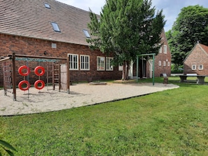 A playground with swings and climbing structures, a brick building with windows, and a grassy area.