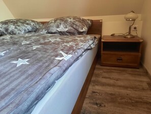 Um quarto com uma cama coberta por um edredom estampado com estrelas, uma mesa de cabeceira de madeira com uma luminária e piso de madeira.