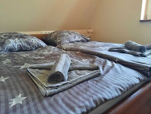 A neatly made bed with star-patterned bedding and rolled towels.