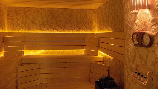 A sauna with wooden benches, a wall-mounted clock, and a shelf with bottles. - Room 1 - Lakeland oasis Reppist (Senftenberg)