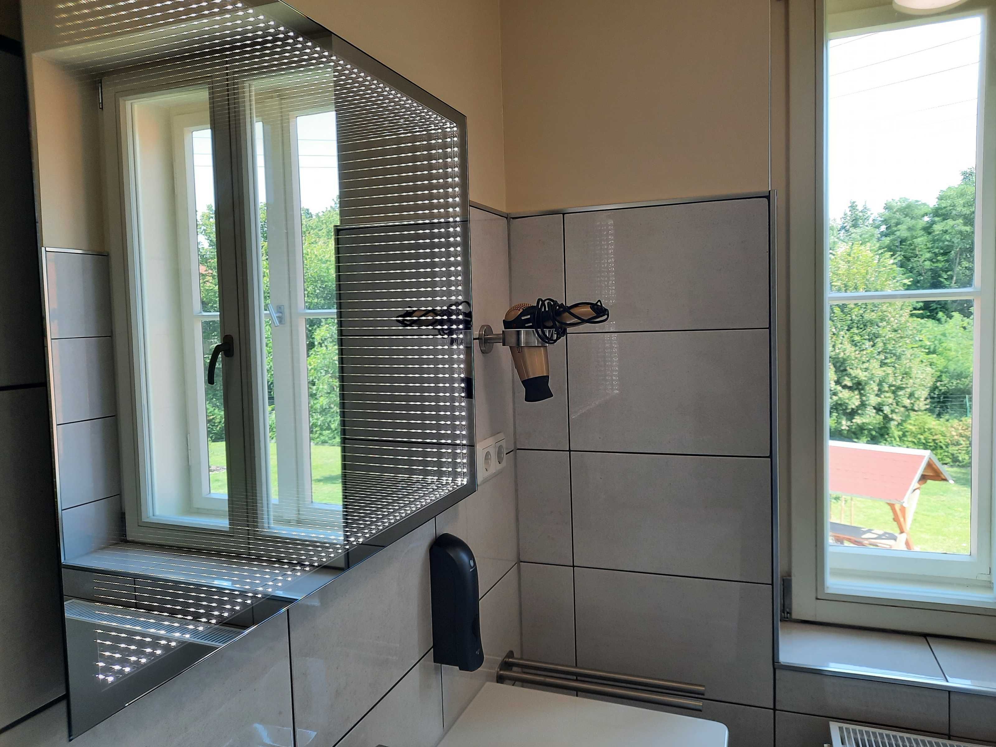 A bathroom with a large mirror, a towel dispenser, and a window with blinds.