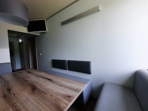 A modern room with a wooden table, a grey sofa, and a flat-screen TV mounted on the wall.