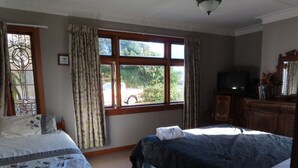 Een slaapkamer met twee bedden, een raam met gordijnen, een televisietoestel en een dressoir.