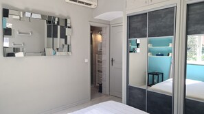 Een slaapkamer met een bed, een garderobe met spiegels, een badkamer met een wastafel en een deur naar een gang.