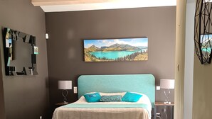 Una habitación de hotel moderna con una cama grande, dos mesitas de noche con lámparas, un televisor montado en la pared y un cuadro de un paisaje.