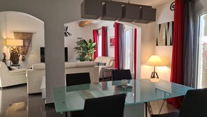 Una sala de estar moderna con una mesa de comedor de vidrio, un sofá color beige y cortinas rojas.
