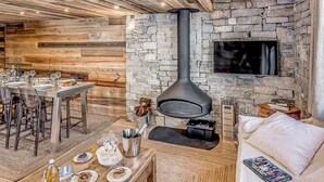 A modern living room with a stone wall, a fireplace, a dining area with a table set for four, and a sofa with a magazine.