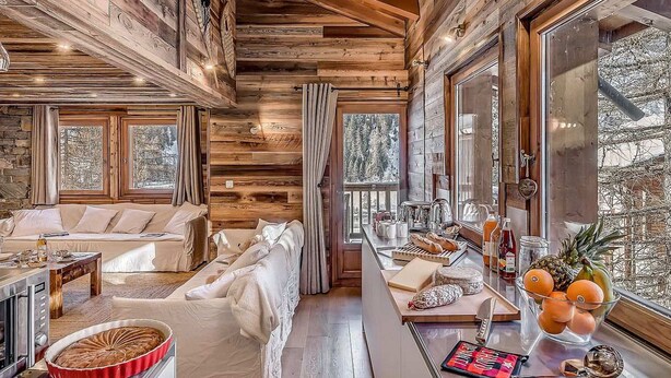 A cozy cabin interior with a wooden interior, a sofa, a dining table with food items, and a kitchen area.