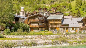 A chalet-style hotel with multiple balconies, stone walls, and a view of a lake.