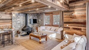 A cozy cabin interior with a stone fireplace, wooden walls, a sofa, and a dining area.