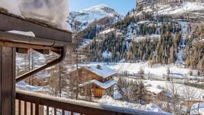 A wooden balcony with a view of a snowy mountain landscape, including a cabin and a river.