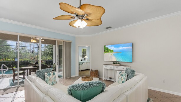 A living room with a white sectional sofa, a ceiling fan, a flat-screen TV, and a view of a pool and outdoor area. - 14090 Oasis w/ Pool, Near Beach (Fort Myers)