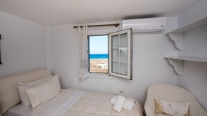 Un dormitorio con una cama, una silla, una ventana con vistas a la playa y un equipo de aire acondicionado.