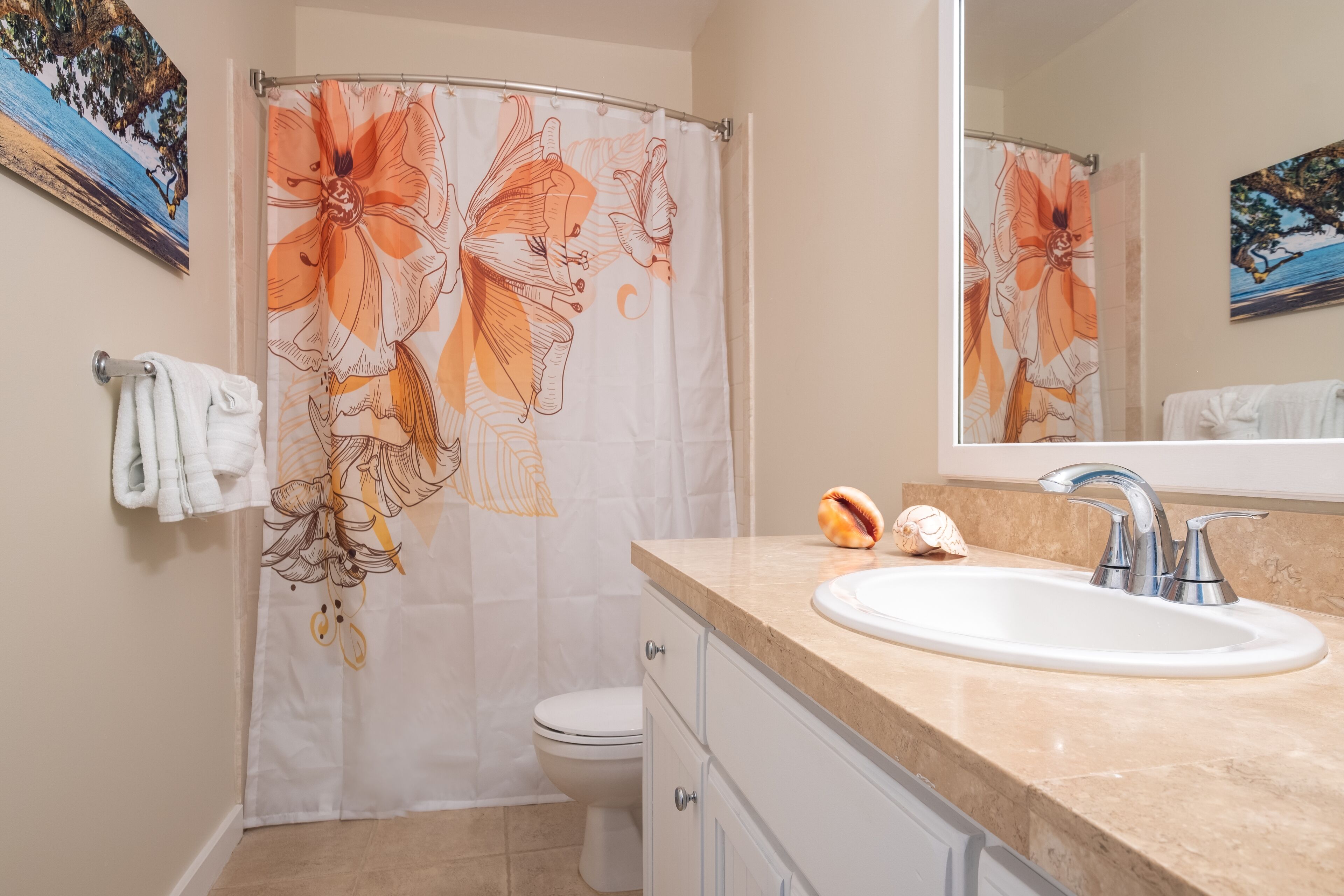 Een badkamer met douchegordijn met bloemenprint, een witte wastafel met spiegel erboven en een handdoekrek met een witte handdoek.