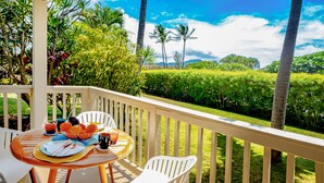 A balcony with a table set for breakfast, surrounded by lush greenery and palm trees.