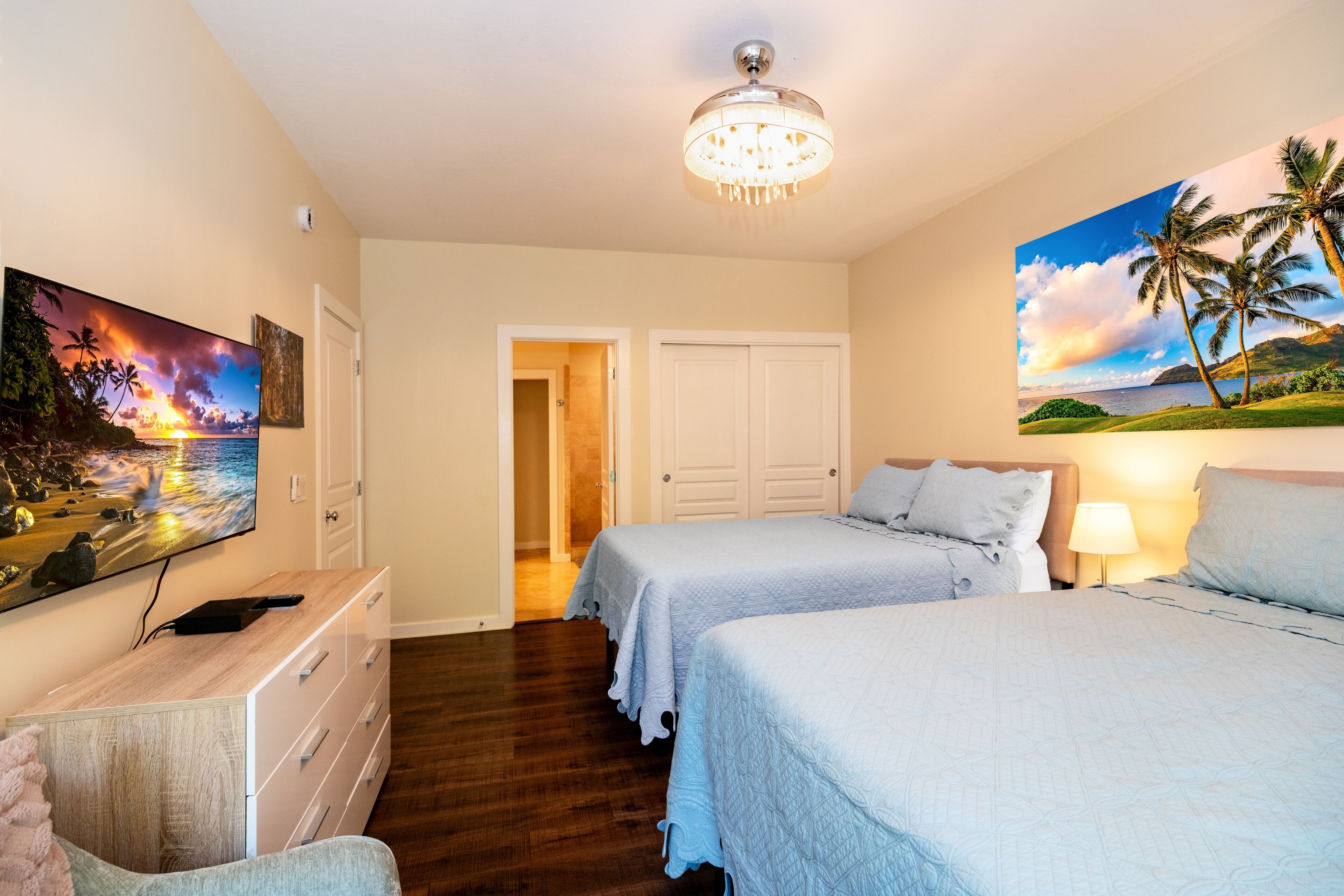 Una habitación de hotel con dos camas, un televisor, un aparador y un cuadro de un atardecer.