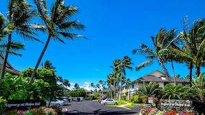 A street view of Regency at Poipu Kai with a clear blue sky, palm trees, and residential buildings.